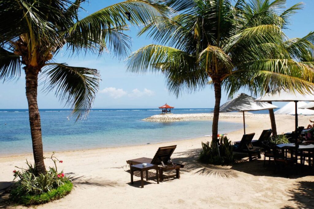 Beach view with palm trees, lounge chairs, and gazebo in Sanur, Bali during Yoga and Meditation Retreats