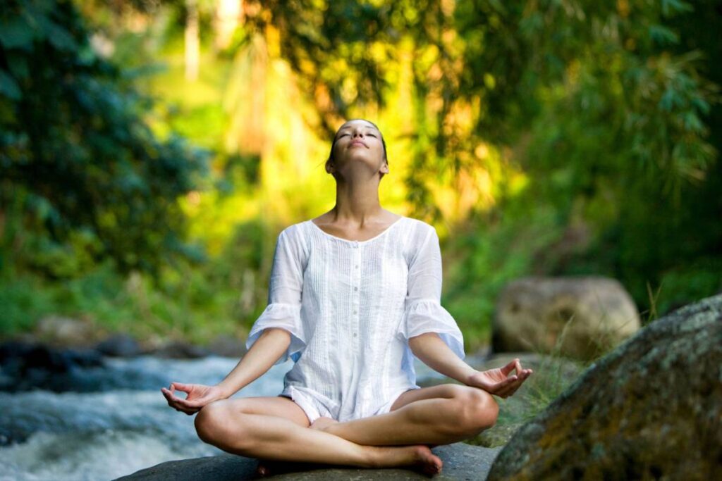 Power of Now Oasis Woman in white practicing meditation by a river in a lush Bali forest