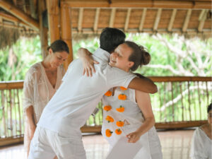 Yoga Teacher Training graduate in white clothing with marigold garland hugging a teacher during the graduation ceremony at the bamboo shala in Sanur, Bali