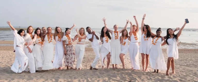 Group of Yoga Teacher Training students and teachers in white clothing with marigold garlands celebrating on Sanur Beach in Bali