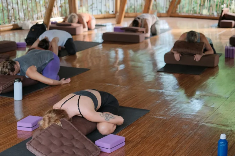 Group of students practicing Yin Yoga in supported Child’s Pose with bolsters and cushions in the bamboo shala at Power of Now Oasis in Sanur, Bali