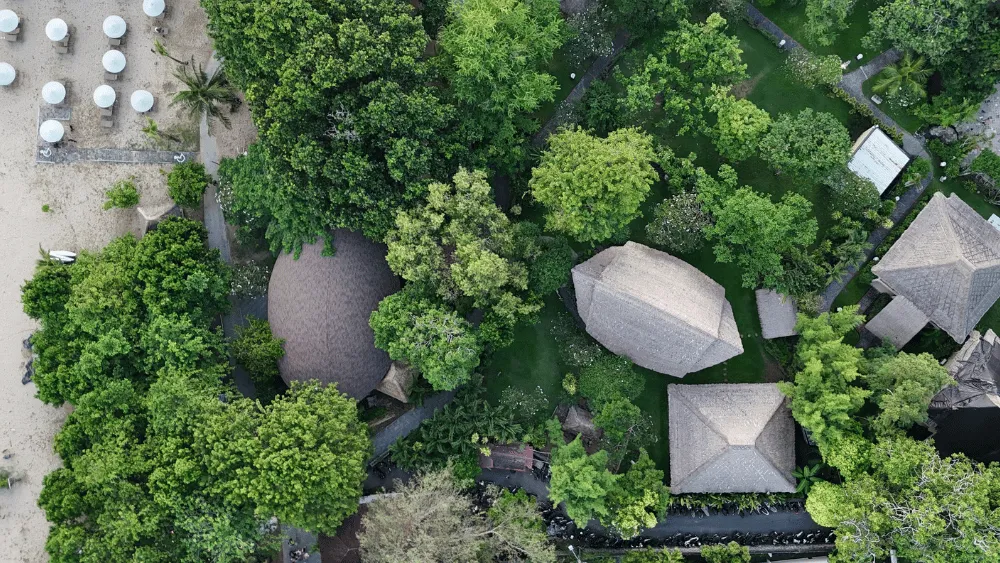 A drone shot of Power of Now Oasis, a yoga and wellness retreat center in Sanur, Bali, surrounded by lush greenery and located near the beach.