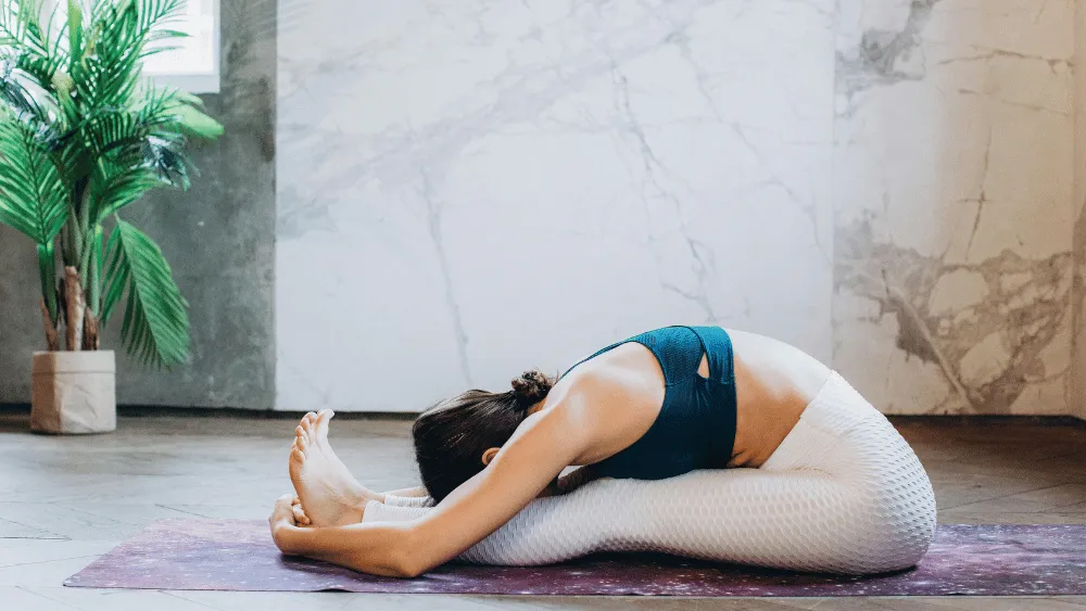 Woman practicing a seated forward bend pose on a yoga mat indoors during a Yin Yoga session