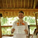 Yoga Teacher Training graduate at Power of Now Oasis in Bali holding certificate and smiling after completion ceremony