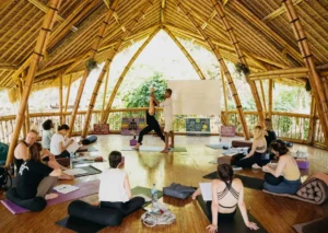 Yoga teacher adjusts a student in a warrior pose during a theory class at Power of Now Oasis in Bali