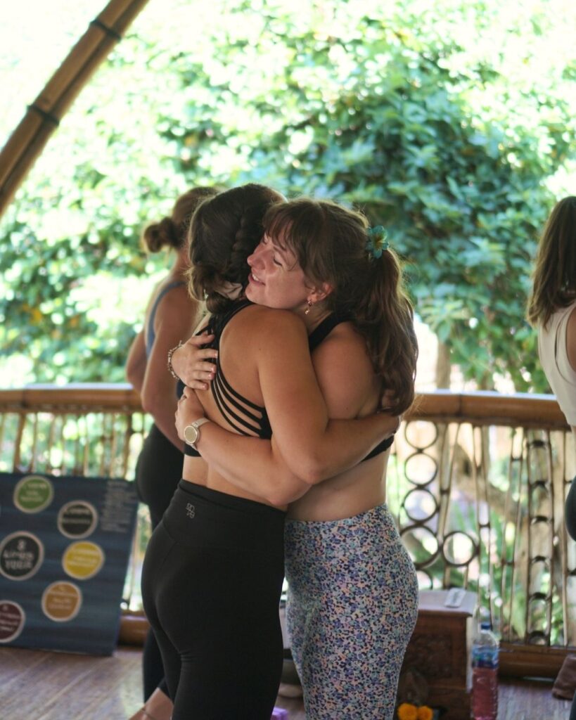 Two yoga teacher training students share a warm hug during the emotional closing ceremony at Power of Now Oasis in Bali