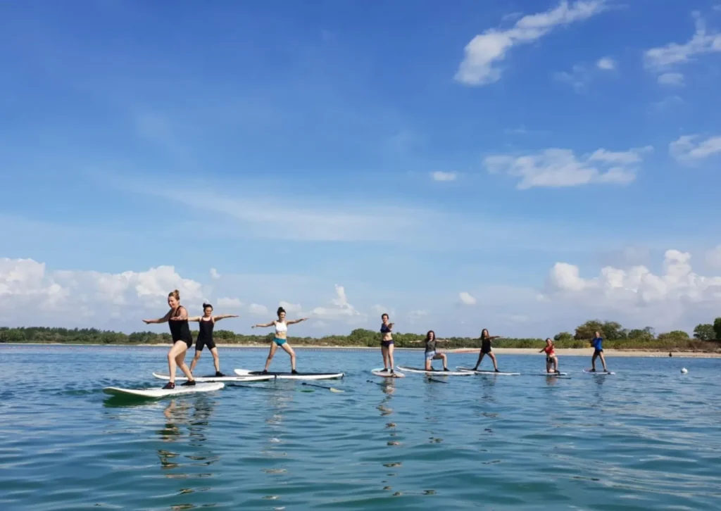 Yoga teacher training students practicing warrior pose on stand-up paddleboards in the ocean