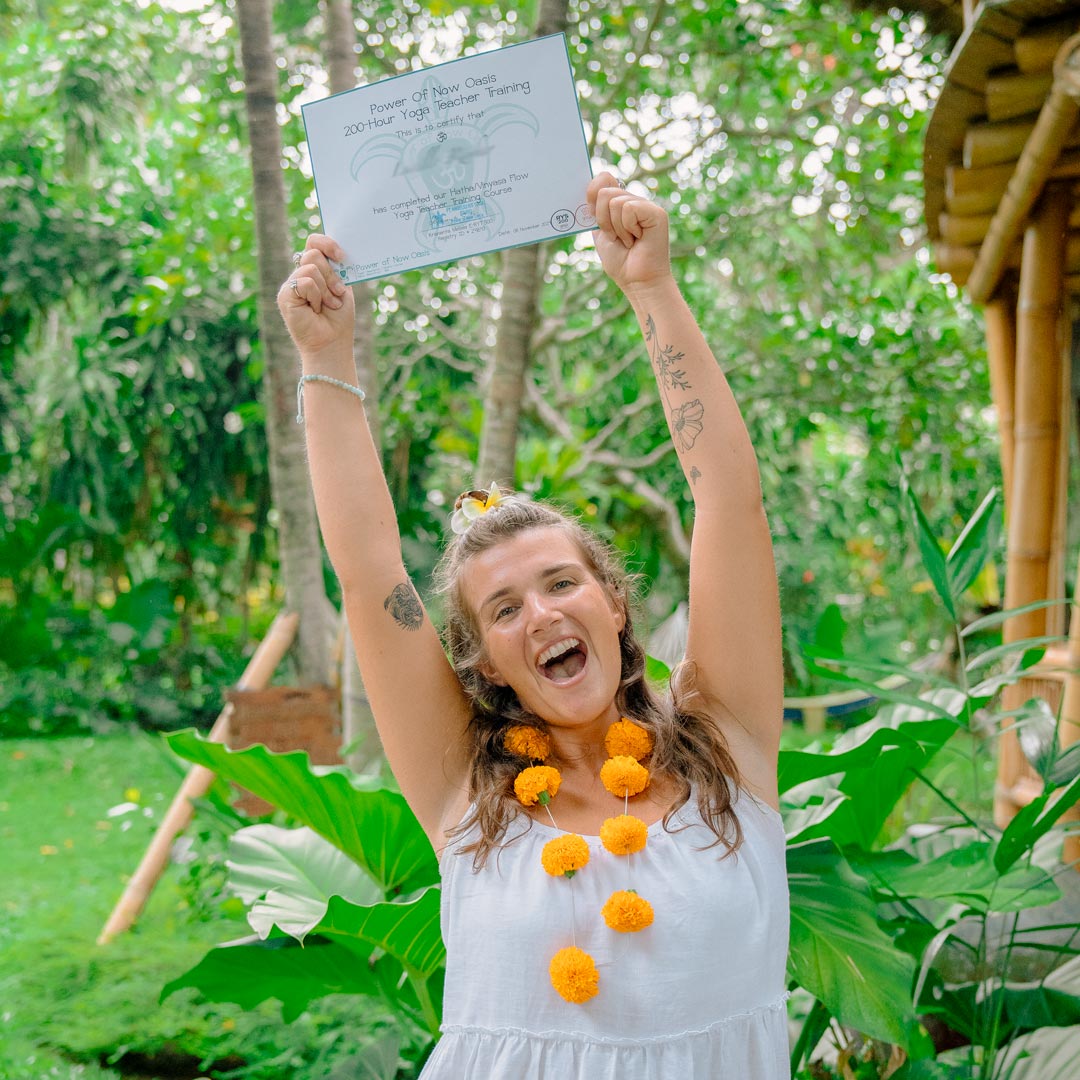 Happy Yoga Teacher Training graduate at Power of Now Oasis in Bali holding certificate and celebrating in tropical garden