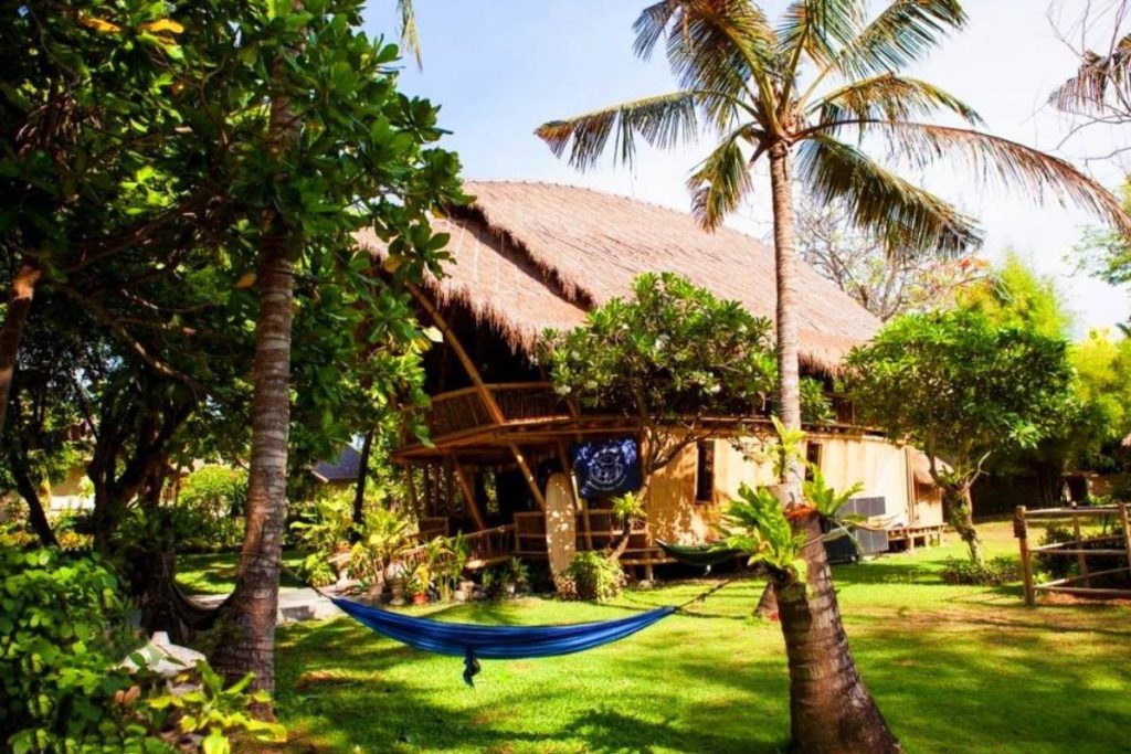 Tropical Bali retreat setting with a thatched roof bamboo building, palm trees, and a hammock in a lush garden