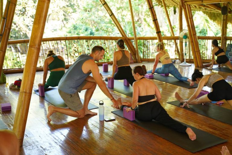 Ricardo guiding a student through a seated forward stretch during a yoga class at Power of Now Oasis, Sanur Bali